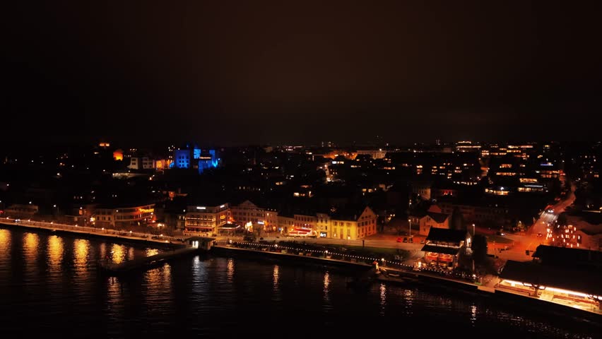 Aerial view of Nyon Castle and the waterfront, illuminated at night creating a warm glow contrasting the dark sky, Nyon, Vaud, Switzerland.