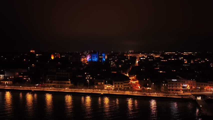 Aerial view of the illuminated Chateau de Nyon standing out in the night skyline, casting a blue glow over the city, Nyon, Vaud, Switzerland.