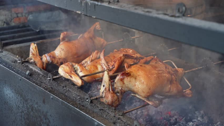 Whole ducks roasting on rotating spits over charcoal grill at street food stall