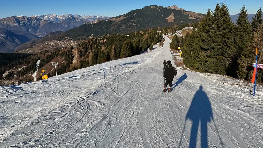 Following Skier Downhill on Wide Sunny Piste with Panoramic Mountain View and Ski Lifts in Background Italian Alps Resort Folgaria