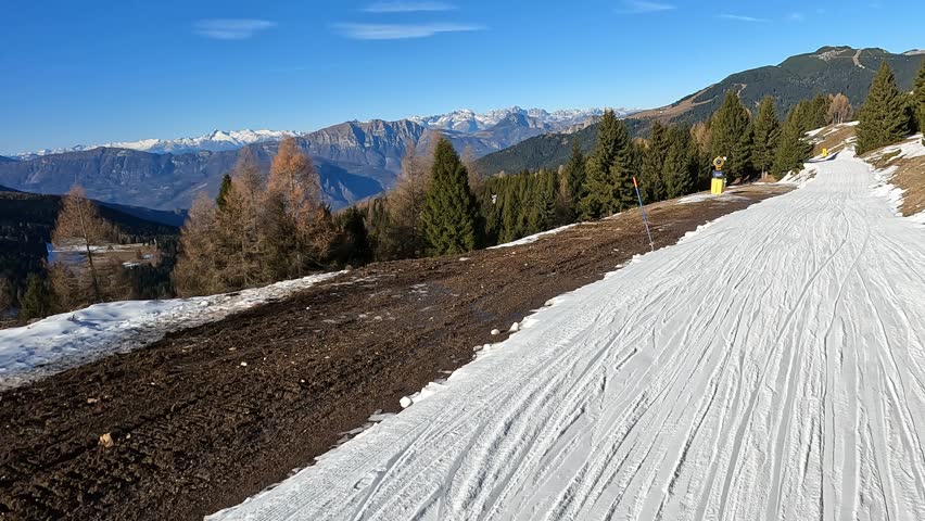 Sunny Ski Piste with Groomed Snow and Visible Ground on Edge showing Late Season Conditions in Alpine Mountain Resort Folgaria