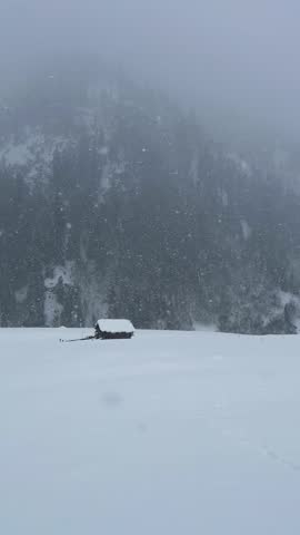 Cinematic Distant View of Log House and Forested mountain covered by clouds in heavy snow
