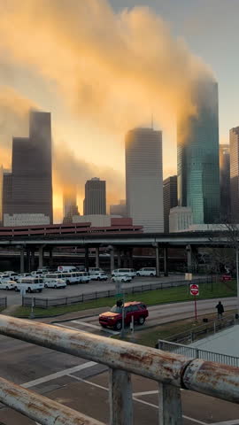 Fog moves through downtown Houston at sunrise in a dramatic time lapse. Backlit clouds wrap around skyscrapers, creating a cinematic urban scene with warm morning color.