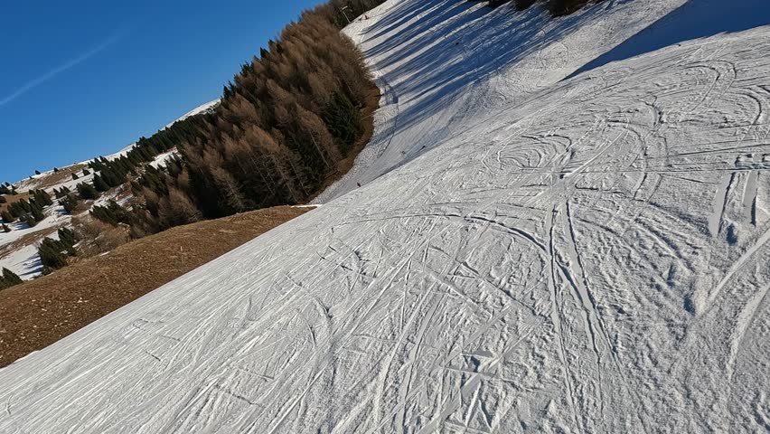 First-person perspective of skiing on a groomed run with visible ski tracks and skier