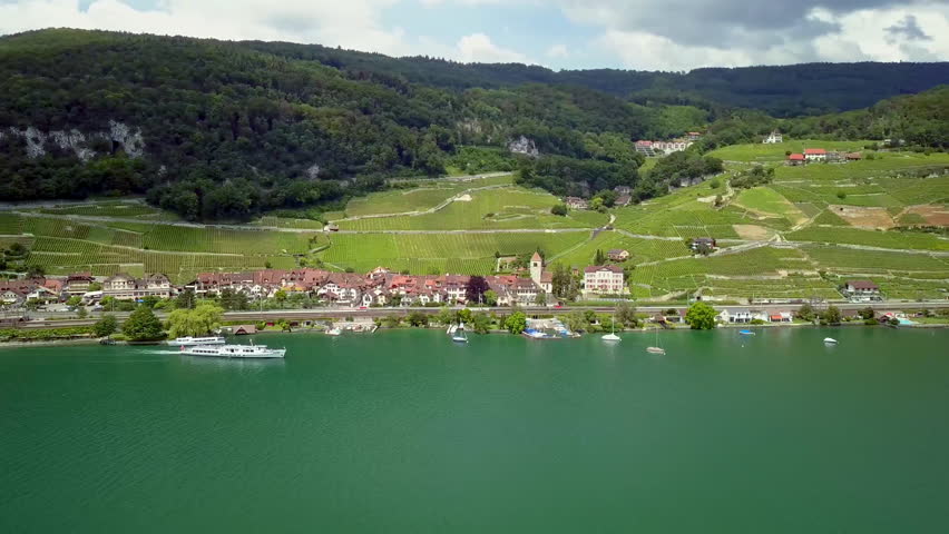 Aerial drone footage over Lake Biel in summer, featuring an island, a large passenger ship and surrounding lake scenery