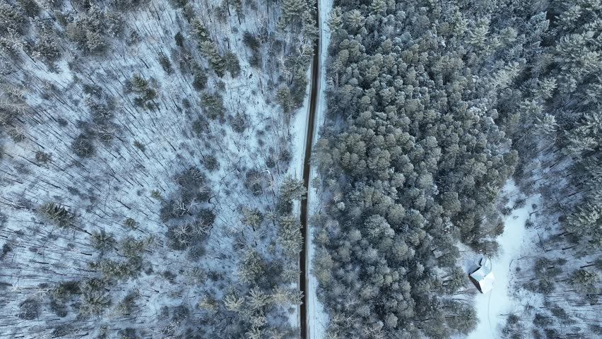 A top-down aerial shot over the Adirondack Mountains, showing a straight road bisecting a dense, snow-covered forest during a winter storm.