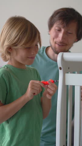 Father and son assembling a baby crib together for their soon arriving son and brother. Family teamwork, bonding, parenting support and preparation for newborn concept.
