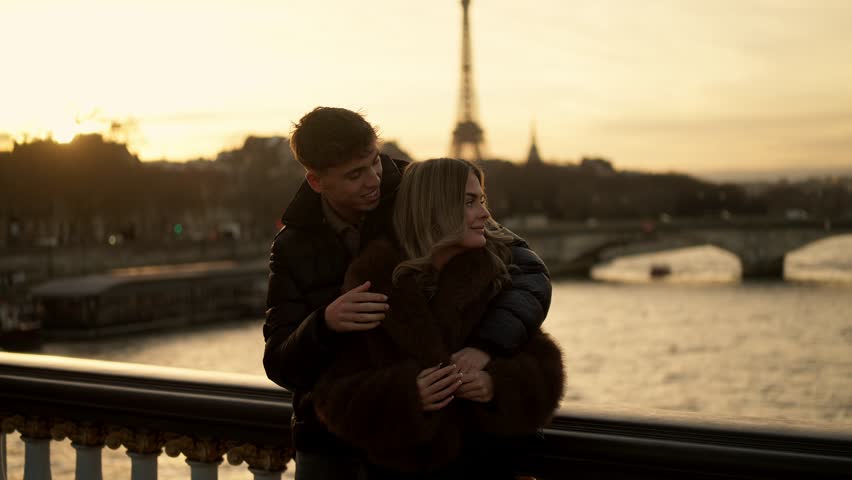 A romantic couple embraces with the Eiffel Tower in the background in Paris France at sunset The golden hour light creates a warm and loving atmosphere The scene captures love affection and the beauty