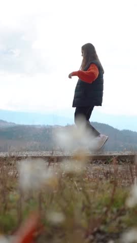 A beautiful young European woman strolls outdoors high in the mountains with an incredible view. A mountain walk and hike on the weekend for relaxation and recharge. Nature and flowers in a field