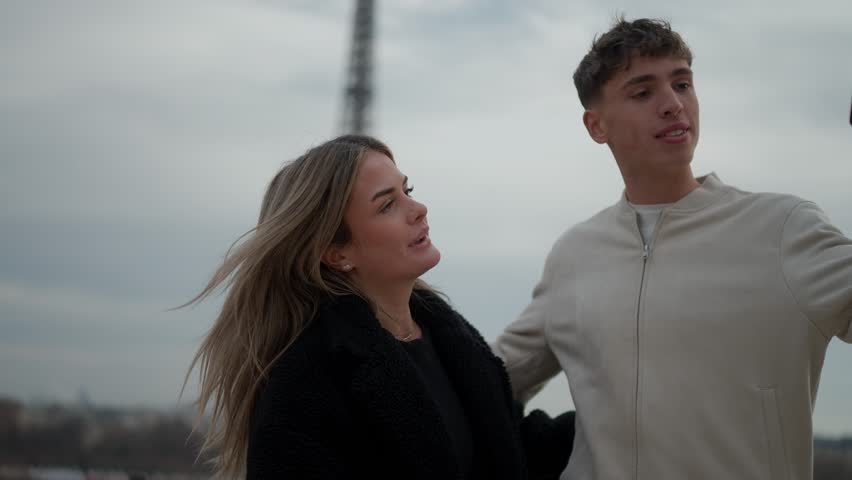 A young couple takes a selfie with the Eiffel Tower in Paris France The man and woman are embracing and smiling as they pose for a photo with the iconic landmark in the background The scene captures a
