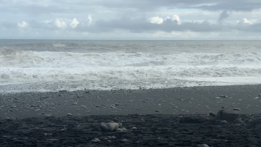 Vast Black Sand Beach with Powerful Crashing Waves under Cloudy Sky in Iceland. High quality 4k footage
