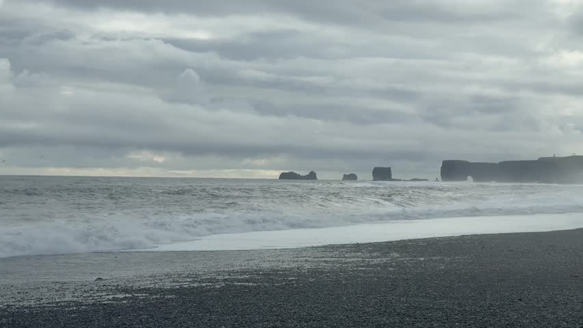 Moody Black Sand Beach with Distant Waves under Heavy Clouds in Iceland. High quality FullHD footage