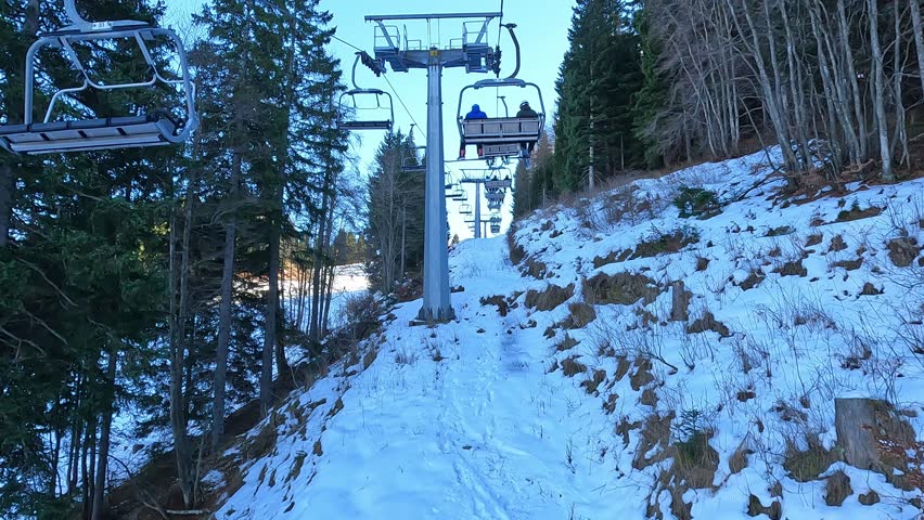 Scenic view from a moving chairlift ride in a winter ski resort with snow covered pine trees and blue sky background perfect for mountain vacation and alpine tourism concepts in high quality 4K.
