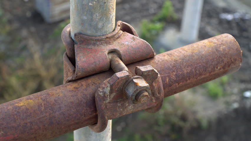 An old rusty clamp makes a joint between pipes on a scaffolding structure