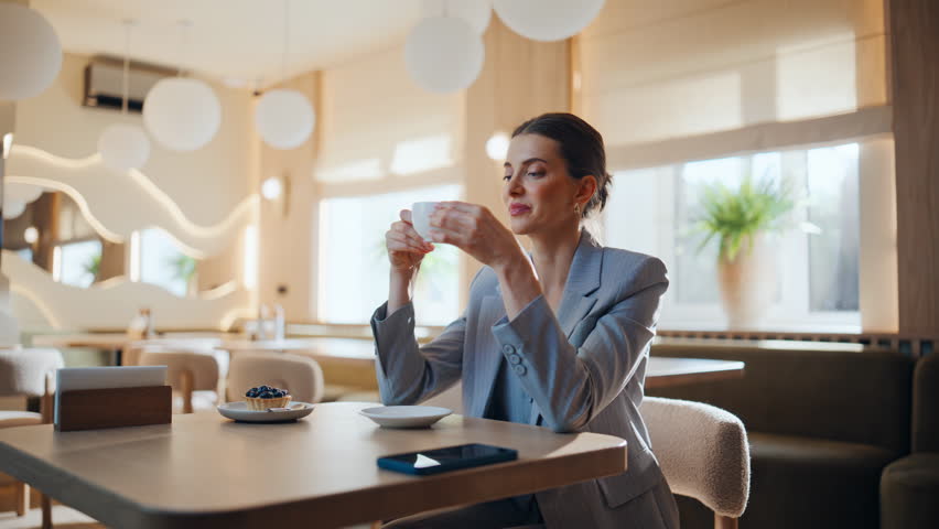 Elegant lady sipping coffee sitting restaurant table closeup. Confident businesswoman relaxing alone in cozy cafeteria. Relaxed woman resting in modern cafe enjoying hot beverage. Free time concept