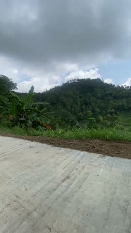 Scenic view of lush green hills under a dynamic cloudy sky in a rural area.