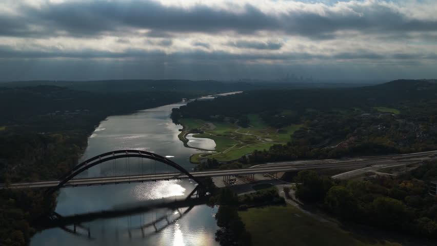 Aerial Views of Pennybacker Bridge Over Glassy Colorado River Reflecting Clouds and Distant Downtown Skyline