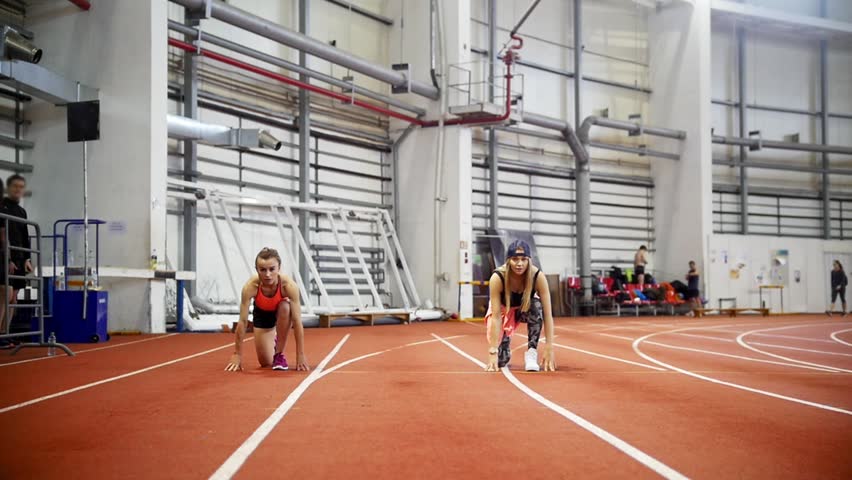 Two female athletes starting sprint race on indoor track