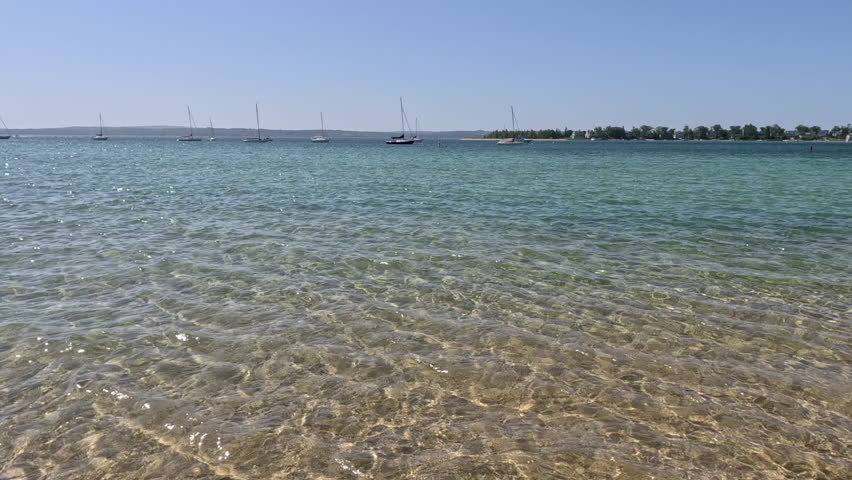 Boats and Beach in the Harbor on Lake Michigan. Panning views of of the crystal clear lake water in a bay on Lake Michigan in Northern Michigan, USA.  Sailboats and a beach are in the distance.