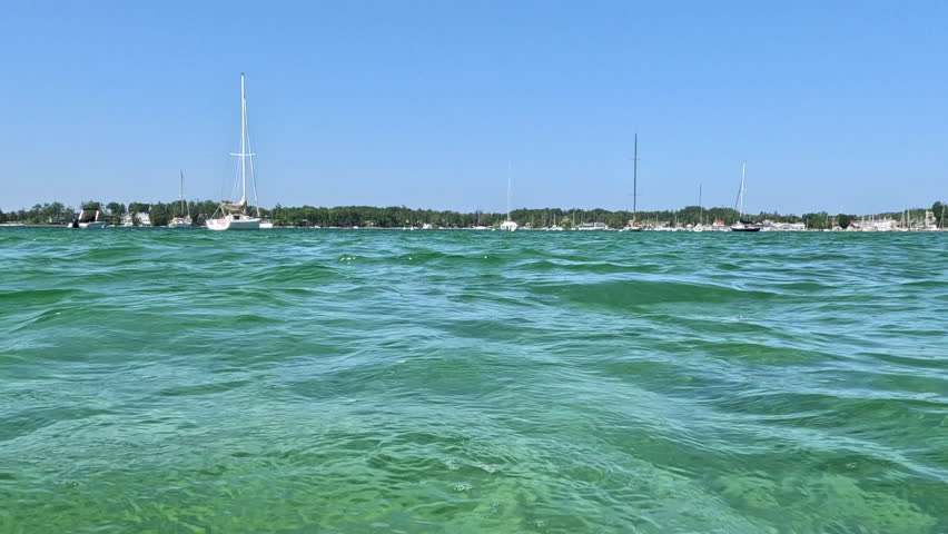 View into Land from a Beautiful Bay of Water on Lake Michigan. Surface level views of the crystal clear lake water in a bay on Lake Michigan in Northern Michigan, USA. Boats and a beach are in the distance.