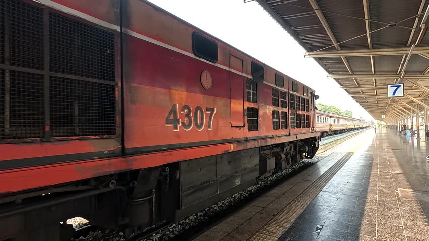 Slow pan along vintage red locomotive and passenger car at sunlit Bangkok railway platform