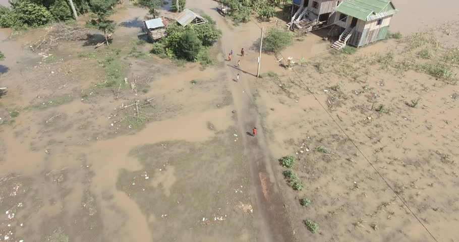 Aerial view of people wading through floodwater in a rural village.