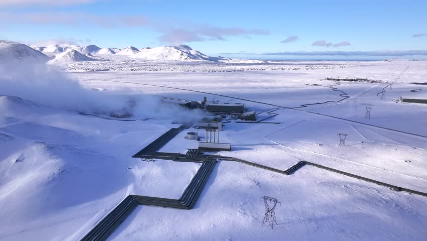 A geothermal power plant in a snowy icelandic landscape, steam rising, clear blue sky, aerial view 4k