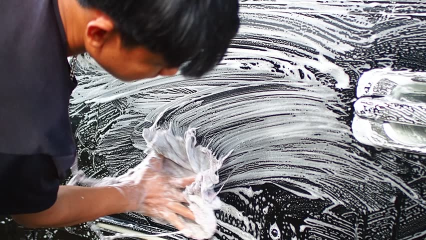 Person washing a black car with a sponge and thick white soap suds