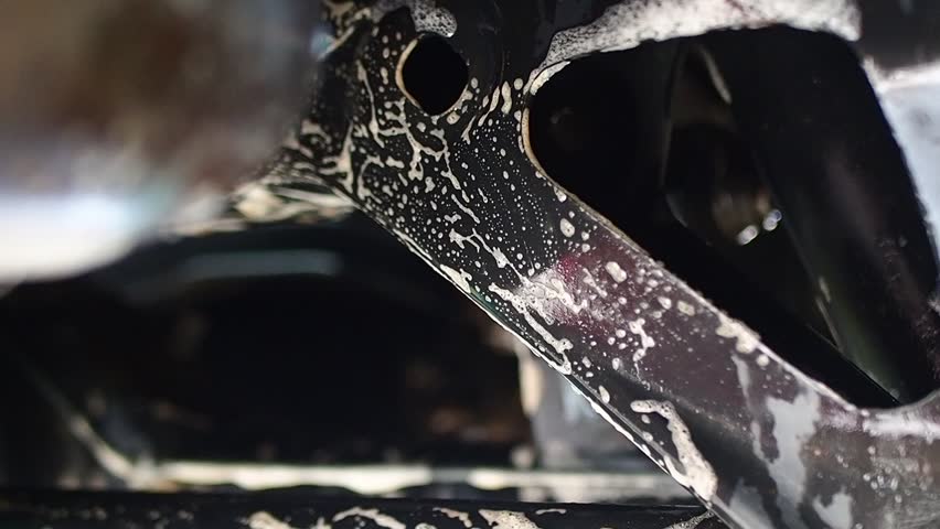 Close-up of Black Metal Vehicle Frame Being Cleaned with White Soap Foam and Suds