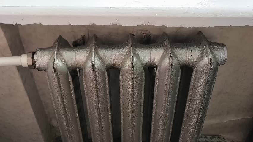 A woman hangs a towel on an old heating radiator. High temperature, heat in the house. Dry indoor air. Old Battery