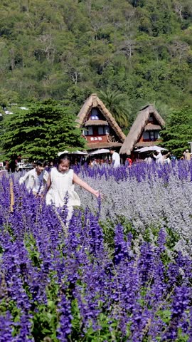A young boy and girl run through vibrant purple blossoms with traditional houses behind them