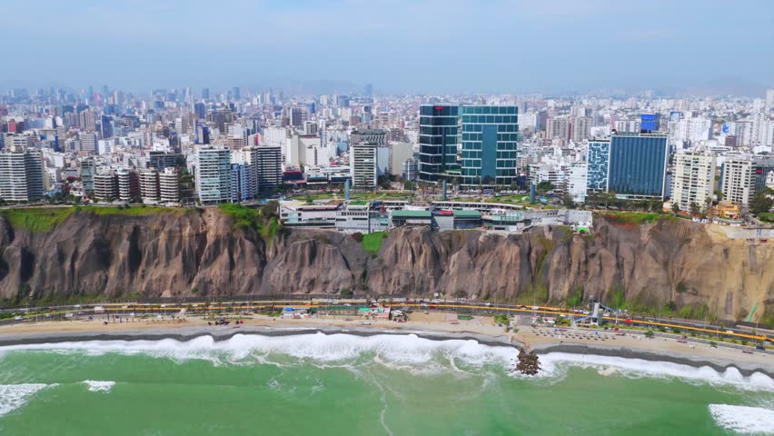 Sunny morning Miraflores Barranco Barranquito Playa Makaha beach pier aerial drone Lima Peru clear hazy blue skies cars traffic surf waves ocean seaside residential skyscraper buildings left motion