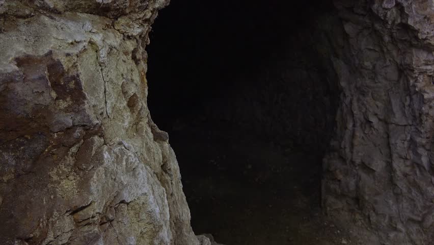 Mysterious dark cave interior revealing ancient rocky walls and shadowy underground chamber passage. Dramatic creepy cavern hall with textured stone formations creating eerie atmospheric environment.