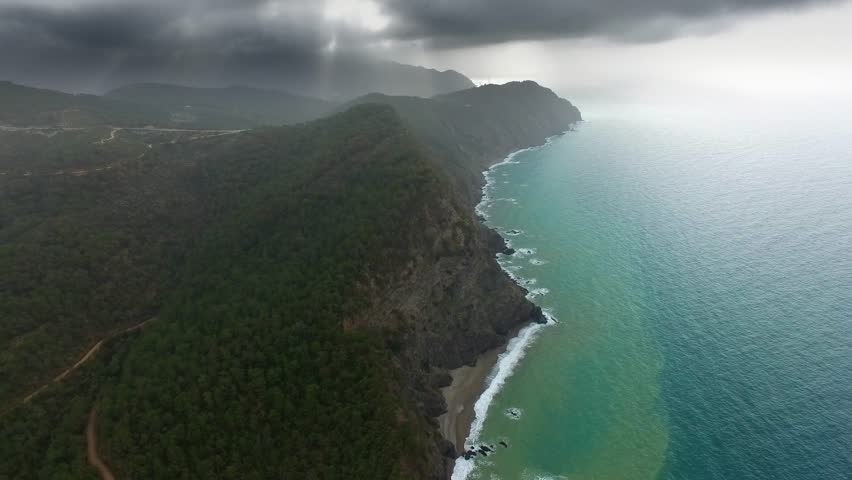 Cinematic aerial view of dense forests meeting turquoise sea along rugged mountainous Patagonia coastline Chile. Dramatic coastal landscape reveals wild nature, remote shores, and vast South American scenery.
