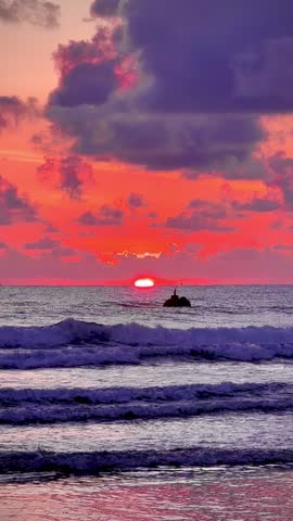 Stunning tropical beach sunset with purple and pink clouds reflecting on the wet sand and calm ocean waves.