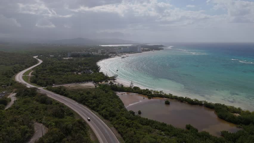 Wide Aerial view of a beach in Falmouth, Jamaica, showcasing turquoise waters, white sand, and lush coastal scenery.