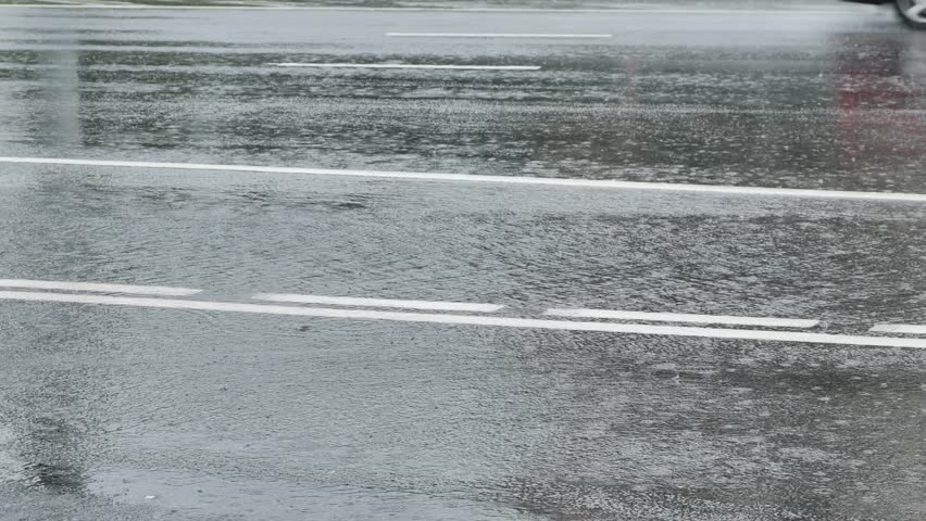 Car driving on wet asphalt road, creating splashes during heavy rain
