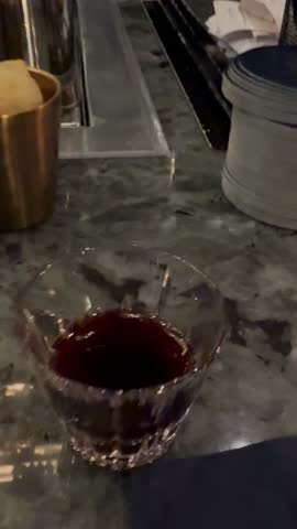 Stylish vertical POV video from a woman at an exclusive bar. Artistic social media-style capture of signature mixology: a pink cocktail in a tall stemmed glass (wine glass) is playfully rotated, and a vibrant red exotic drink in a small rocks glass. Gourmet bar snacks include potato chips and olives with sauce in elegant copper cups, served with a fancy pick. The stylish, lively atmosphere shows a blurred background of bartender action and bar tools. Perfect for content about luxury travel, nightlife, cocktail culture, gourmet blogging, high-end advertising, and celebrating special moments. Shot in a trendy, first-person perspective ideal for Reels, Stories, and Shorts.