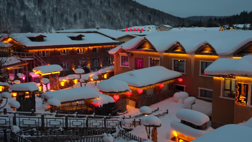 The view of Snow Town in Harbin, China, is stunning during a snowstorm, with snow covering the rooftops, and the city is beautifully illuminated at night.
