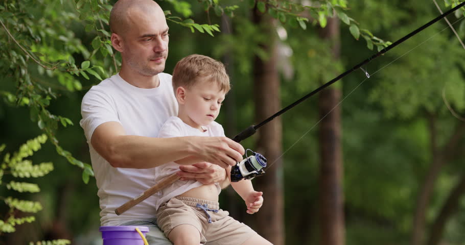Loving father shouts with delight at small movement of rod. Dad helps preschooler blond son pull fishing rod with care and joy. Man whispers words of support