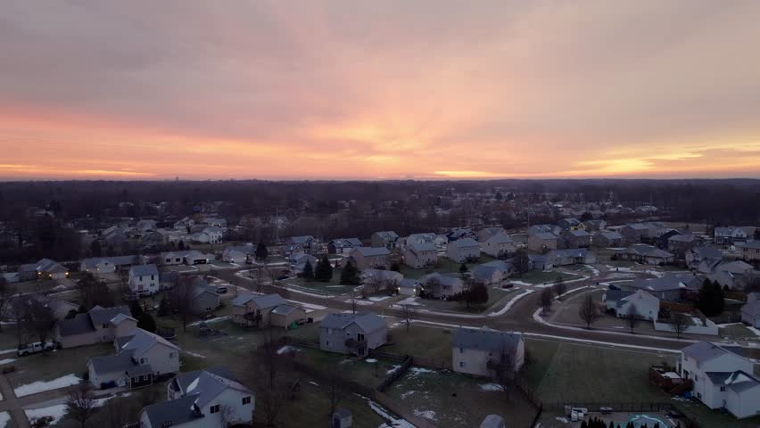 4K aerial drone footage of a vibrant winter sunrise over suburban neighborhoods in Grand Rapids, Michigan, featuring snow-covered rooftops, colorful skies, and calm morning atmosphere.