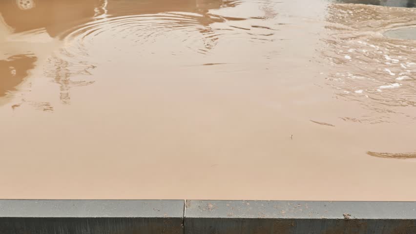 Car driving through flooded urban street splashing muddy water during heavy rain