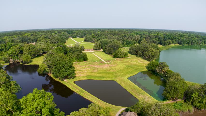 Drone footage of multiple small water ponds surrounded by green grassy fields and farmland near Charleston South Carolina
