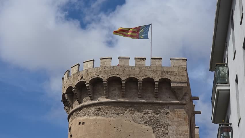 view of The flag of Valencia (Reial Senyera)  and the Torres de Quart (Quart Towers), one of the two remaining gates of the old city wall of Valencia, Spain.