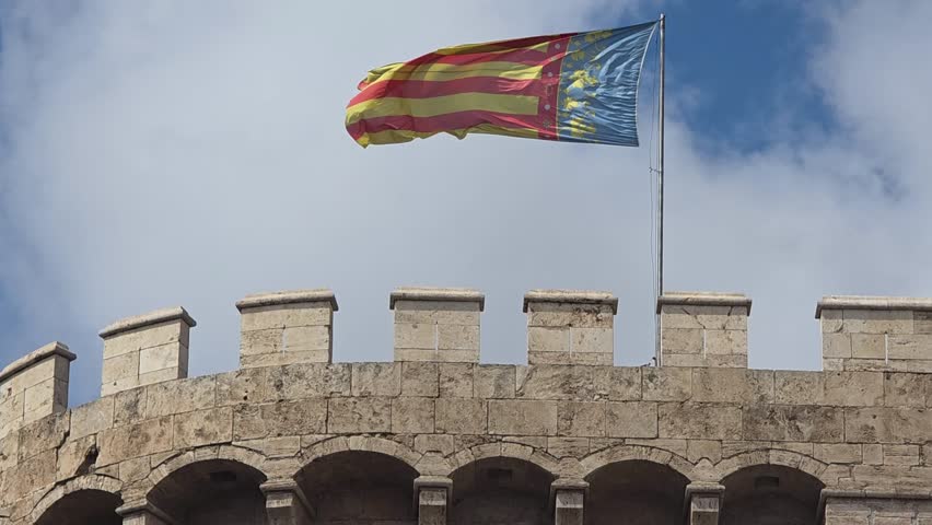 view of The flag of Valencia (Reial Senyera)  and the Torres de Quart (Quart Towers), one of the two remaining gates of the old city wall of Valencia, Spain.