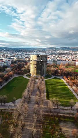 Aerial portrait drone shot panning right over the Augarten Tower in Vienna at winter sunset, showing the skyscraper, surrounding city buildings, and streets bathed in warm sunlight under clear skies.