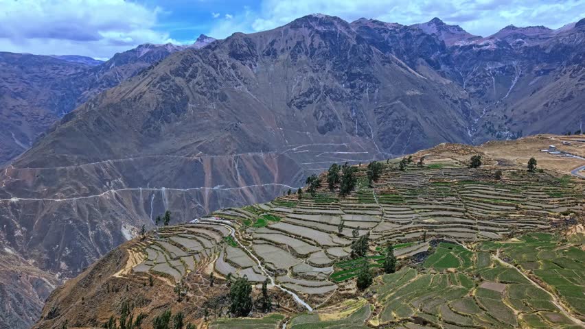 Reverse-moving drone pulls away from canyon edge to reveal layered terraced farmland as the full height and power of Colca Canyon’s mountainscape emerges, including the dramatic opening of the canyon