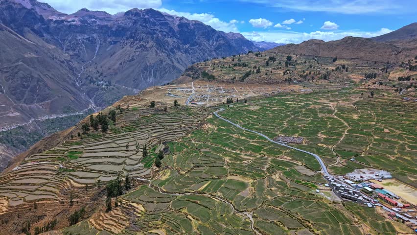 Epic aerial view of layered agricultural terraces clinging to the edge of Colca Canyon Peru. Precise geometric patterns contrast with the immense canyon drop and surrounding Andean mountains.