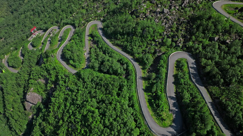 Top-down aerial view of Trollstigen hairpin turns in Norway. The winding road cuts through forested mountains, showcasing engineering and natural beauty.