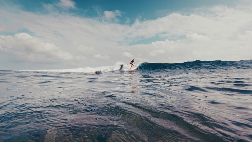 Surfer rides the ocean wave in the Maldives with another surfer diving with surf board underwater. In water and underwater view of the surfer on the wave